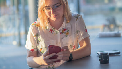 Kvinna sitter vid ett bord och tittar på sin mobil som hon håller i handen.
