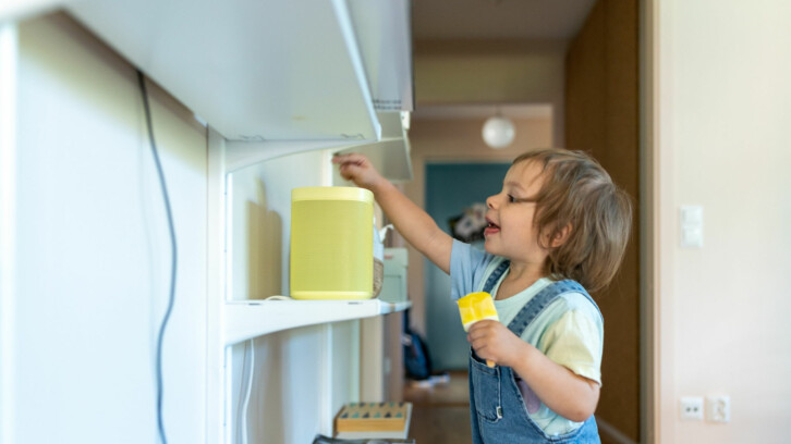 Ett litet barn med en glass i handen sträcker sig mot en smart högtalare.