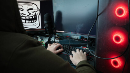 En person sitter framför en dator, på skärmen syns en elak figur.