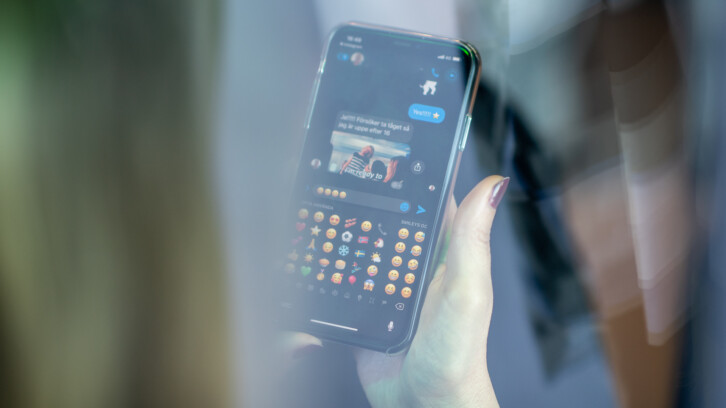 En person håller en mobil i handen, på skärmen syns emojis.