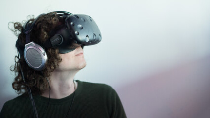 Man med VR-glasögon och hörlurar står framför vit bakgrund.