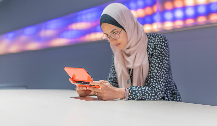 Ung kvinna sitter med en surfplatta framför en vägg med neon-lampor.