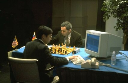 Kasparov vs Deep Blue vid ett bord med blå duk och chackbräde på.